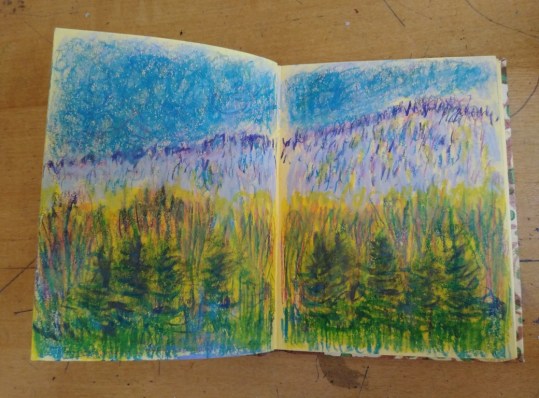 view of trees in front of foothills with blue, violet and green artist's crayons in tiny handmade sketchbook